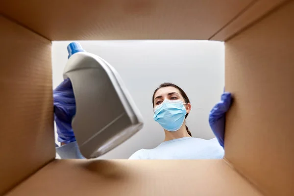 Woman in mask taking cleaning supplies from box — Stock Photo, Image