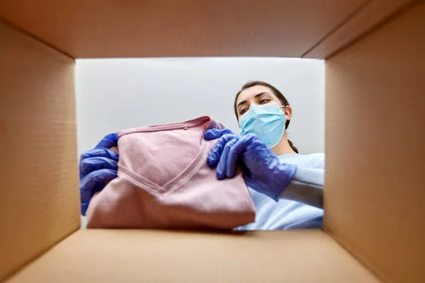 Vrouw in masker openen pakket doos met kleren — Stockfoto