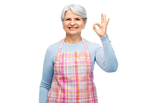 Leende äldre kvinna i förkläde visar ok gest — Stockfoto