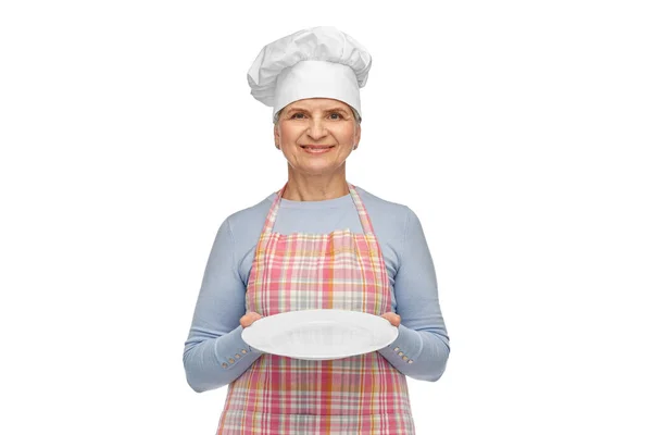 Smiling senior woman or chef holding empty plate — Stock Photo, Image