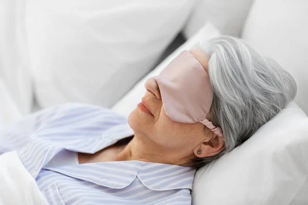 Mulher sênior com máscara ocular dormindo na cama em casa — Fotografia de Stock