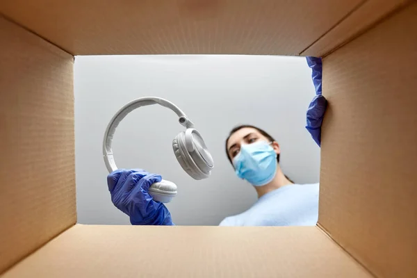 Γυναίκα με μάσκα συσκευάζοντας ακουστικά σε κουτί δεμάτων — Φωτογραφία Αρχείου