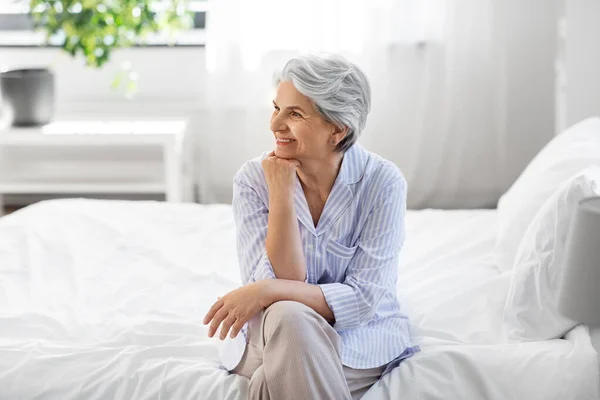 Boldog idős nő ül az ágyon otthon hálószoba — Stock Fotó
