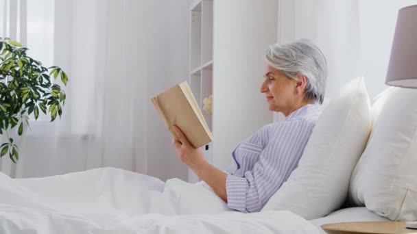 Wanita senior membaca buku di tempat tidur di kamar tidur rumah — Stok Video