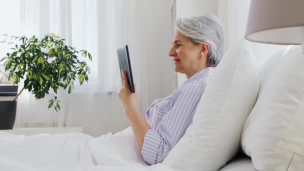 Vieille femme avec tablette pc ayant appel vidéo au lit — Video