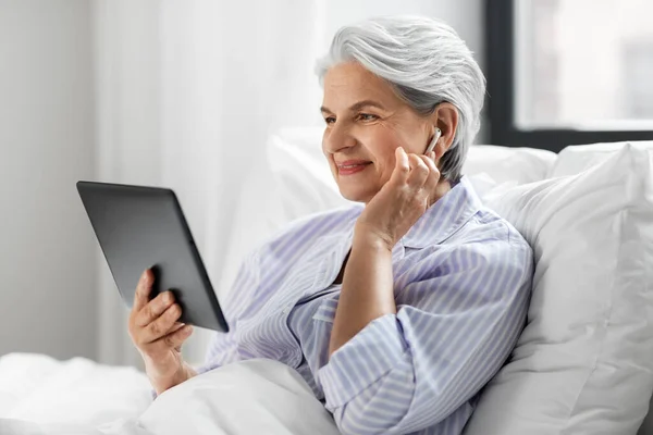 Donna anziana con tablet pc e auricolari a letto — Foto Stock