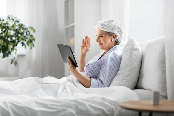 Vecchia donna con tablet pc con videochiamata a letto — Foto Stock
