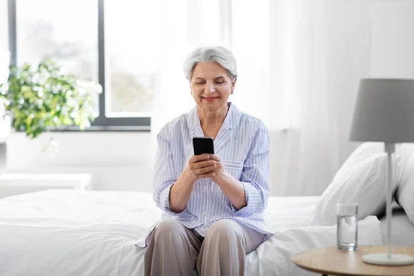 Felice donna anziana con smartphone sul letto a casa — Foto Stock