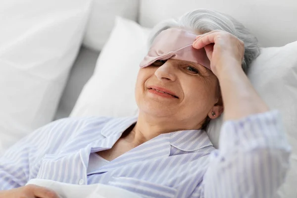 Ηλικιωμένη γυναίκα με μάσκα ύπνου ματιών στο κρεβάτι στο σπίτι — Φωτογραφία Αρχείου