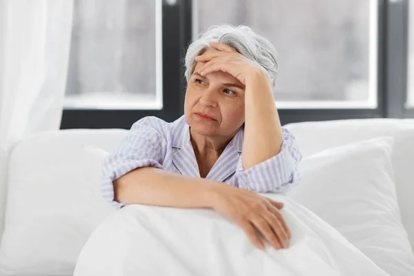 Donna anziana con mal di testa seduta a letto a casa — Foto Stock