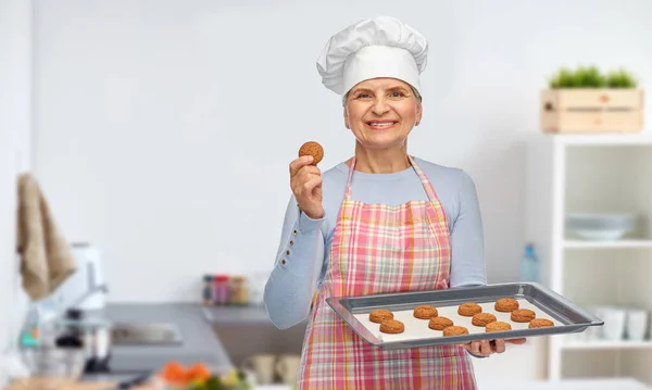 Starsza kobieta w toque z ciasteczkami na patelni — Zdjęcie stockowe