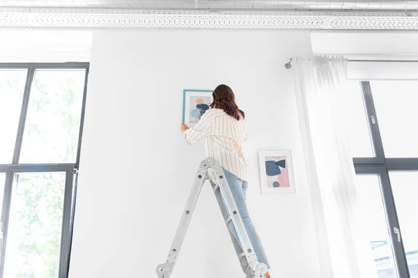 Woman on ladder decorating home with art — Stock Photo, Image