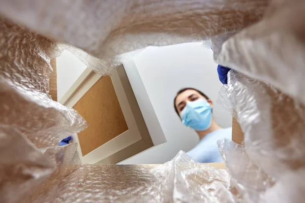 Woman in mask opening parcel box with photo frame — Stock Photo, Image