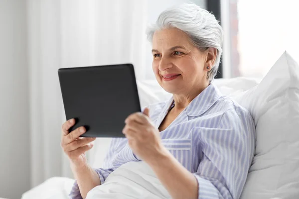 Donna anziana con tablet pc a letto a casa camera da letto — Foto Stock