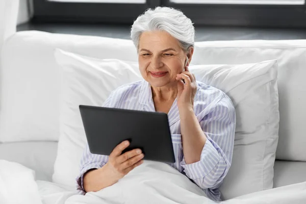 Seniorin mit Tablet-PC und Kopfhörer im Bett — Stockfoto