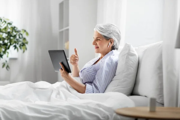 Vecchia donna con tablet pc con videochiamata a letto — Foto Stock