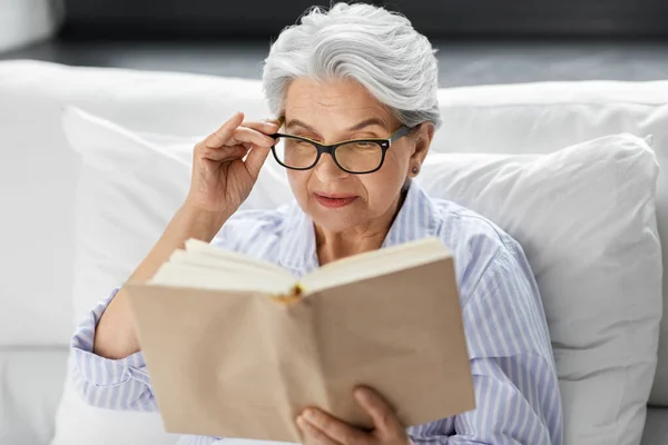 Mulher velha em óculos livro de leitura na cama em casa — Fotografia de Stock