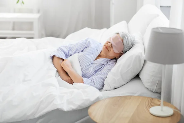 Wanita senior dengan masker mata tidur di tempat tidur di rumah — Stok Foto