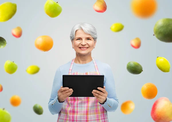 Lächelnde Seniorin in Schürze mit Tablet-Computer — Stockfoto