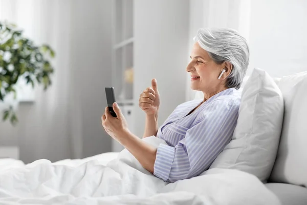 Senior woman with phone having video call in bed — Stock Photo, Image