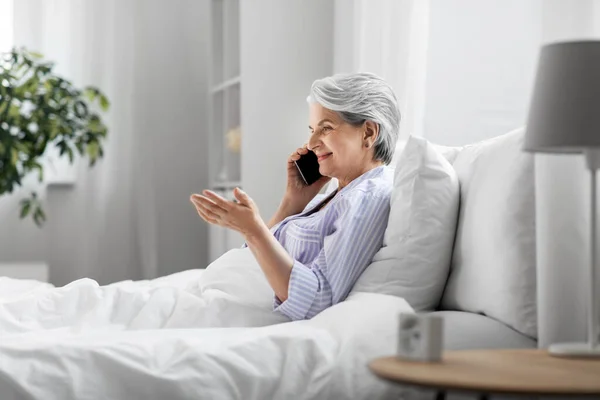 Donna anziana che chiama su smartphone a letto a casa — Foto Stock