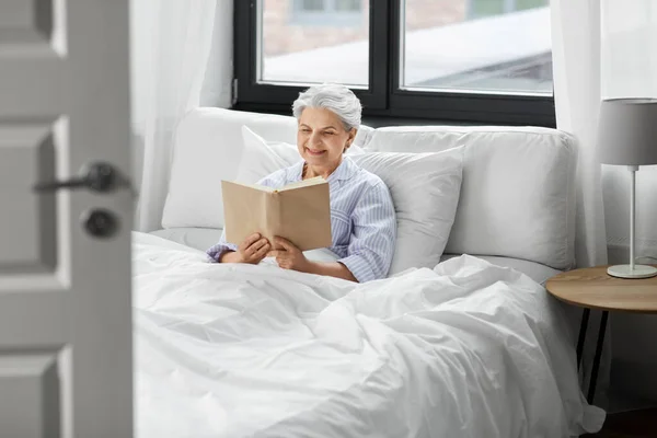 Senior donna lettura libro a letto a casa camera da letto — Foto Stock