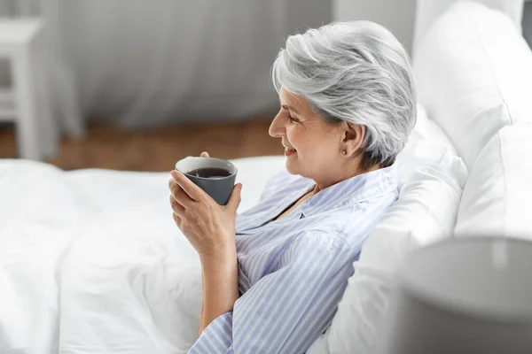 Donna anziana con tazza di caffè a letto a casa — Foto Stock