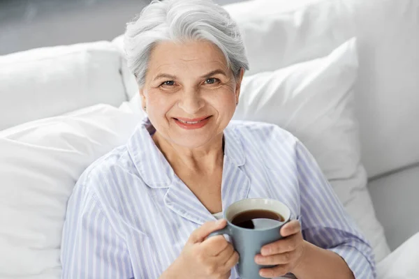 Donna anziana con tazza di caffè a letto a casa — Foto Stock