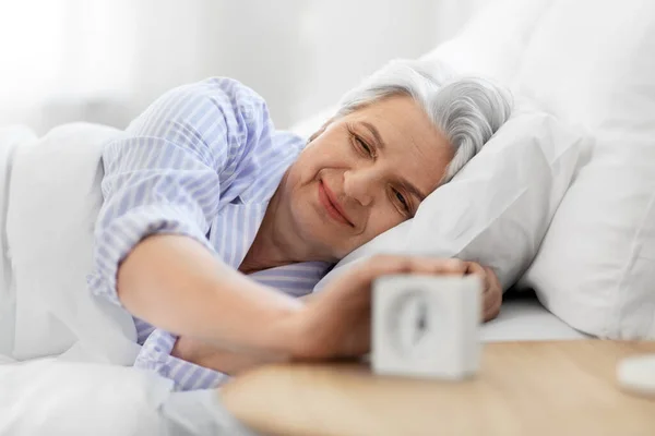 Felice donna anziana con sveglia a letto a casa — Foto Stock