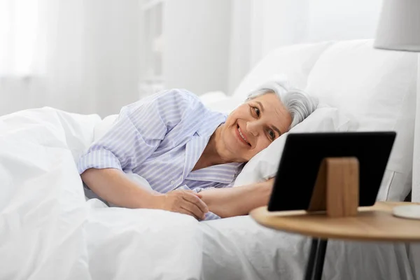 Gelukkig senior vrouw met tablet pc in bed thuis — Stockfoto