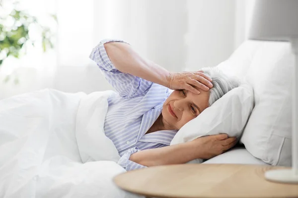 Пожилая женщина с головной болью в постели дома — стоковое фото