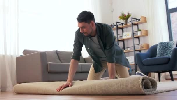 Feliz sonriente joven hombre desplegando alfombra en casa — Vídeos de Stock