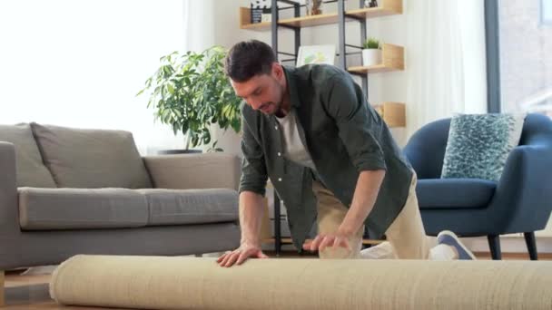 Gelukkig lachende jongeman ontvouwt tapijt thuis — Stockvideo