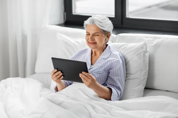 Пожилая женщина с планшетным ПК и наушниками в постели — стоковое фото