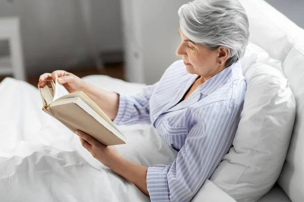 Mulher sênior livro de leitura na cama em casa quarto — Fotografia de Stock
