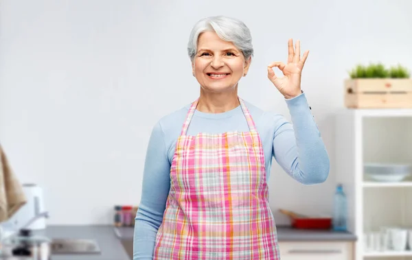 Улыбающаяся пожилая женщина показывает хороший жест на кухне — стоковое фото