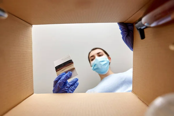 Vrouw in masker uitpakken pakket doos met haarbanden — Stockfoto