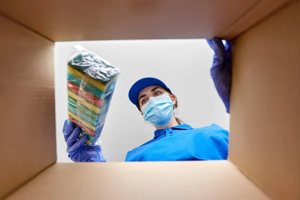 Vrouw in masker verpakking keuken sponzen naar doos — Stockfoto