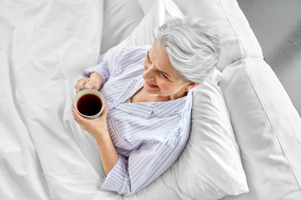 Donna anziana con tazza di caffè a letto a casa — Foto Stock