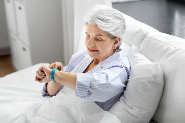 Ευτυχισμένη ηλικιωμένη γυναίκα με ιχνηλάτη υγείας κάθεται στο κρεβάτι — Φωτογραφία Αρχείου