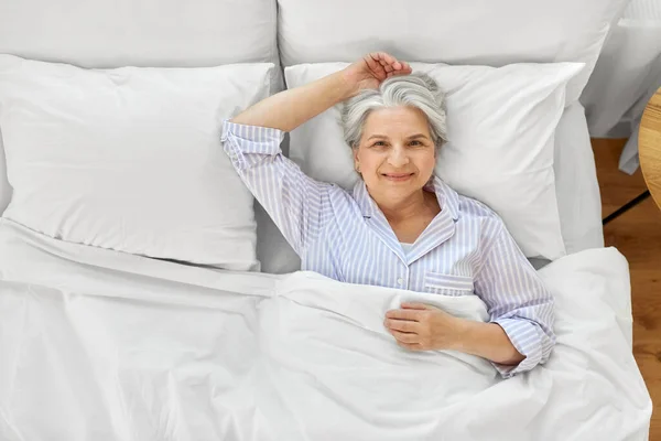 Sorridente donna anziana sdraiata a letto a casa camera da letto — Foto Stock