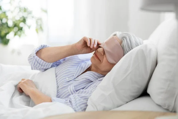 Seniorin mit Augenmaske zu Hause im Bett — Stockfoto