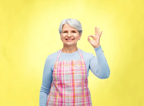 Sorridente donna anziana in grembiule mostrando gesto ok — Foto Stock