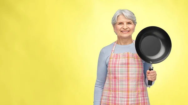 Χαμογελαστή ηλικιωμένη γυναίκα με ποδιά και τηγάνι — Φωτογραφία Αρχείου
