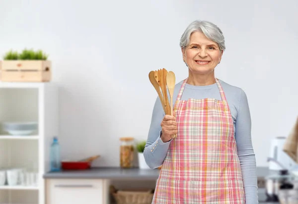 Улыбающаяся пожилая женщина с деревянными ложками на кухне — стоковое фото