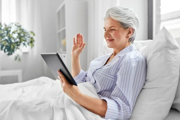 Vecchia donna con tablet pc con videochiamata a letto — Foto Stock