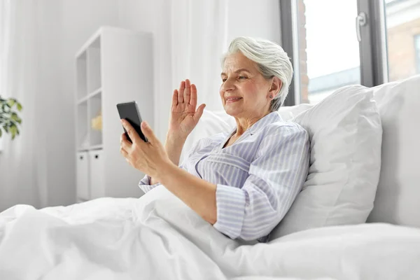 Donna anziana con telefono avendo videochiamata a letto — Foto Stock