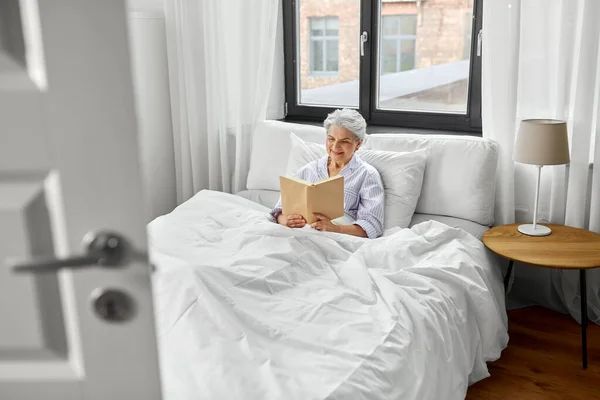 Senior woman reading book in bed at home bedroom — Stock Photo, Image