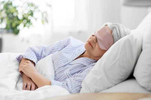 Mujer mayor con máscara para los ojos durmiendo en la cama en casa —  Fotos de Stock