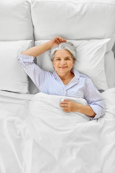 Tersenyum wanita senior berbaring di tempat tidur di kamar tidur rumah — Stok Foto